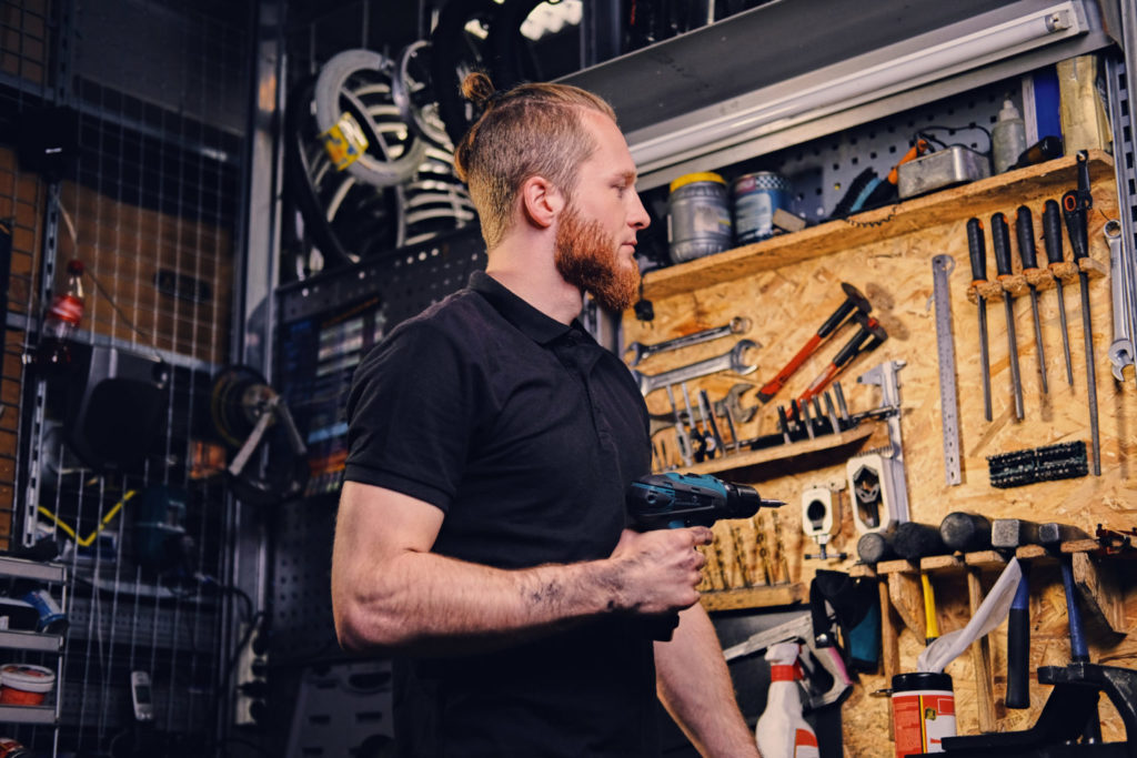 Bicycle mechanic holding screwdriver over bike tools stand in a workshop.